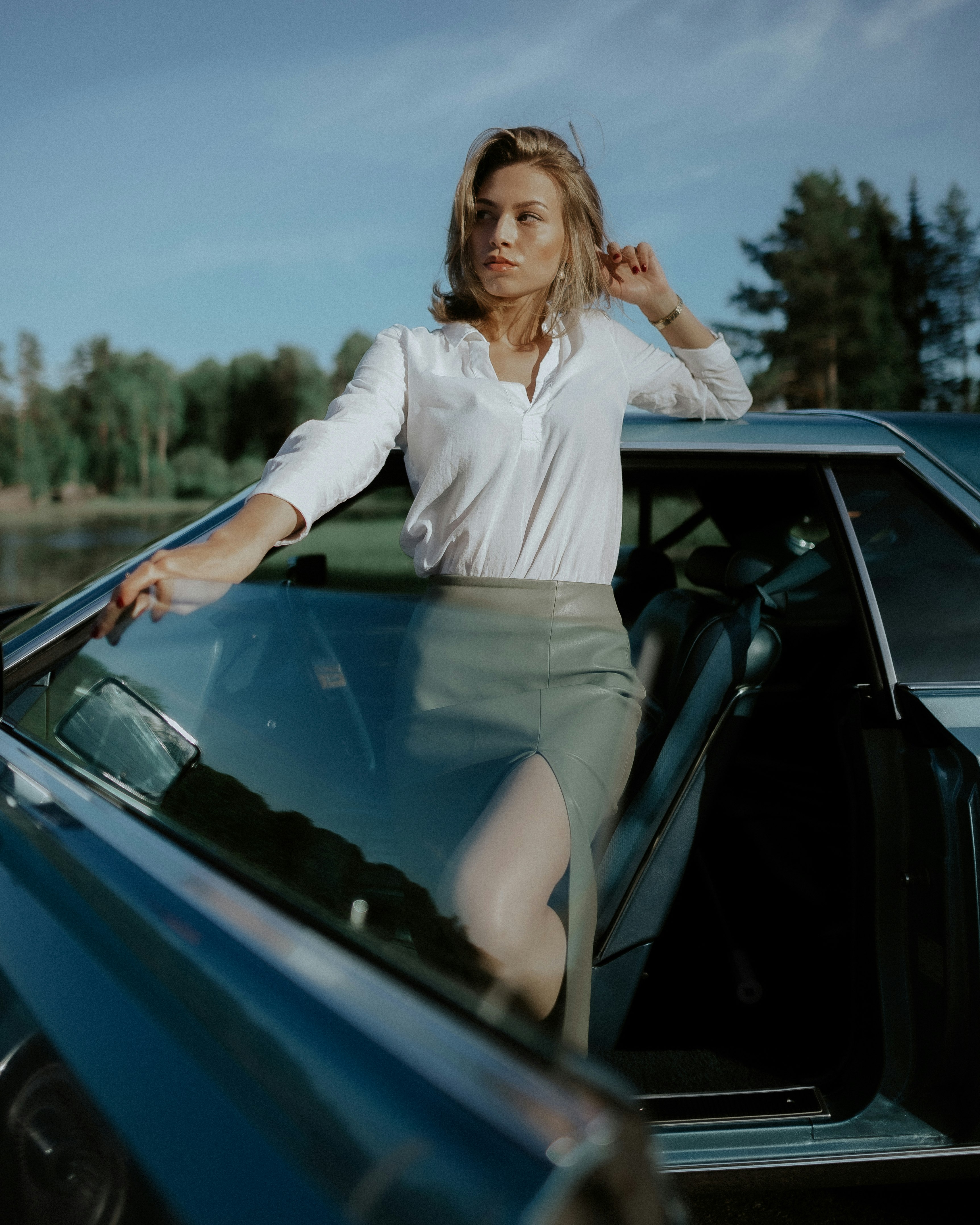 woman in white long sleeve shirt and gray skirt sitting on blue car